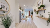Located at 1010 Browning Rd in Lakeland, FL, this single-story, 2-bedroom, 2-bathroom unit features a thoughtfully designed open-concept layout that maximizes its compact footprint. Light wood-style flooring runs throughout the main living areas, creating a cohesive and airy feel, while white walls and recessed lighting contribute to a bright, welcoming atmosphere.

The kitchen and living room share an open, flowing space anchored by white cabinetry with modern hardware, granite countertops, and stainless steel appliances including a full-size refrigerator, range, and microwave. A kitchen island provides additional prep and dining space. French doors at the far end of the living area allow natural light to pour in and offer outdoor views, with a ceiling fan overhead enhancing comfort.

Both bedrooms feature windows with natural light, floating wall shelves, and light flooring. The primary bedroom comfortably accommodates a full-size bed alongside additional furnishings. Each bathroom includes a tub-shower combination with clean white subway tile surround, light wood-toned vanity cabinetry, and granite countertops. A hallway connects the private areas of the unit to the main living space.