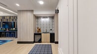 Located at 550 Westlake Park Blvd in Houston, Texas, this generously sized amenity lounge delivers a premium, multi-functional entertainment experience across a single, open floor plan. The space is defined by contemporary design elements, including coffered and tray ceilings with integrated LED lighting, light wood flooring, and a refined neutral palette accented by bold pops of yellow and blue.

The main lounge area features plush sectional sofas, vibrant yellow accent chairs, and sleek coffee tables arranged around a large flat-screen TV, with a stylized shelving display wall serving as a striking focal point. A boldly patterned accent wall adds texture and visual interest throughout. Adjacent to the lounge, a bar counter with gold-toned barstools and built-in greenery offers a social gathering hub, separated from the billiards area by an elegant slatted wood and metal room divider. A full-sized pool table anchors this entertainment zone beneath a statement geometric pendant light fixture.

Large floor-to-ceiling windows along one side of the space invite abundant natural light and offer views of the surrounding greenery. Intimate café-style seating nooks provide quieter spaces for conversation or work. A dedicated golf simulator room, finished in dark tones with turf flooring and a Full Swing projection screen, rounds out the offerings, making this amenity space a comprehensive destination for recreation and relaxation.