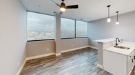 Located in Manchester, NH, this thoughtfully designed 2-bedroom, 1-bathroom residence offers a functional and modern living experience across a single floor. The open-concept kitchen and dining area serves as the heart of the home, featuring white shaker cabinetry, stainless steel appliances including a French door refrigerator and electric range, a striking quartz countertop with veined marble-like patterning, a matte black faucet, and pendant lighting. A peninsula with a white quartz surface provides additional workspace and a natural divider between the kitchen and dining area. Large floor-to-ceiling windows in the dining and living area flood the space with natural light and offer expansive views of the Manchester skyline, complemented by a ceiling fan overhead. Wood-look luxury vinyl plank flooring runs through the main living areas, while both bedrooms are fitted with patterned carpet. Each bedroom includes a closet with built-in shelving. The bathroom is clean and contemporary, with white cabinetry, a quartz vanity top, matte black hardware, and a conveniently stacked washer and dryer unit integrated into the space. The overall aesthetic is clean, modern, and move-in ready.