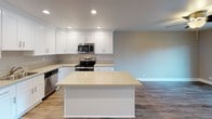Located on the third floor at 22432 Center St in Castro Valley, California, this single-level apartment offers a well-designed open-concept layout with contemporary finishes throughout. The kitchen serves as a central highlight, featuring crisp white shaker cabinetry, light quartz countertops, a center island with additional prep space, stainless steel appliances including a range, microwave, and dishwasher, and recessed lighting overhead. Wood-look laminate flooring flows seamlessly through the kitchen and main living areas, providing a warm, cohesive aesthetic. The living space benefits from natural light and access to an outdoor area, as seen through sliding glass doors. The bedrooms are finished with plush wall-to-wall carpeting, neutral taupe walls, and ceiling fans with integrated lighting for year-round comfort. Each bedroom includes baseboard heating and windows that invite natural light and views of the surrounding neighborhood. The bathroom is thoughtfully appointed with a full tub-and-shower combination, white cabinetry with brushed nickel hardware, a quartz vanity countertop, and wood-look tile flooring that ties the space together. Clean lines and a neutral color palette throughout the unit create a calm, move-in-ready environment suited for a variety of lifestyles.