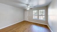 Located at 3800 Weatherstone Park Rd in New Bern, NC, this single-story, 2-bedroom, 1-bathroom home offers a well-organized and functional floor plan with a clean, neutral aesthetic throughout. Warm hardwood-style flooring runs continuously through the living areas, kitchen, and bedrooms, lending cohesion and a welcoming feel to the entire space.

The open-concept living and dining area is bright and airy, with a ceiling fan overhead and a large window that draws in natural light and frames views of the surrounding greenery. This space flows seamlessly into the kitchen, which is divided by a peninsula counter with a built-in sink. The kitchen features white cabinetry with ample storage, a white electric range, refrigerator, dishwasher, and overhead lighting — a fully equipped and efficient cooking space.

Both bedrooms continue the hardwood-style flooring and are fitted with ceiling fans and windows that allow natural light in. The primary bedroom benefits from direct access to the shared bathroom and a dedicated closet with wire shelving for organized storage. The second bedroom also includes a closet and a window with outdoor views.

The bathroom is clean and functional, equipped with a tub-shower combination featuring grab bars and a towel bar. Outside, the home is situated on a well-maintained lot with mature trees, a covered entry, and open green space, offering a peaceful setting.