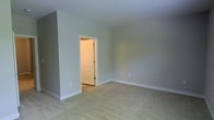This single-floor space presents a clean, understated aesthetic defined by neutral sage-green walls, bright white trim, and soft wall-to-wall carpeting in a warm beige tone. The interior reflects a simple, functional design philosophy with smooth, flat ceilings and well-proportioned rooms that offer flexibility for a variety of uses. The color palette throughout is cohesive and calming, creating a welcoming ambiance that serves as a blank canvas for personalization. White painted interior doors with classic panel detailing add a traditional touch, while the crisp white baseboards provide a polished contrast to the soft wall tones. Electrical outlets are thoughtfully placed throughout, indicating practical layout planning. The open feel of the rooms, combined with consistent flooring and wall finishes, lends a sense of continuity across the space. Overall, the interior presents a well-maintained, move-in ready environment with a neutral and timeless design sensibility suited to a wide range of occupants and furnishing styles.