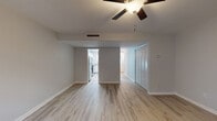 This two-floor residence is designed with a clean, contemporary aesthetic, featuring light wood-style flooring that runs consistently throughout the living areas, bedrooms, and hallways, creating a cohesive and airy feel. Neutral gray walls provide a versatile backdrop, while white trim and baseboards add crisp contrast to each room.

The main living area is generously proportioned, equipped with a ceiling fan and overhead lighting. An open layout connects the living space to adjacent rooms, with a partial wall dividing the living area from a hallway leading to a closet with louvered bifold doors and additional rooms. The kitchen is accessible directly from the living area and features stainless steel appliances, including a range, over-the-range microwave, and refrigerator, complemented by white cabinetry and light granite-style countertops.

The bedrooms are well-sized, each outfitted with ceiling fans and windows fitted with horizontal blinds that allow natural light to filter in. The bathroom presents a clean, all-white design with a tub-shower combination, white subway tile surround, a single-sink vanity with under-cabinet storage, a framed mirror, and light-bar above. A staircase connects the two floors, as seen in the 3D overview, with the upper level mirroring the light, open character of the lower floor.