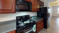 Located at 113 Cherry Court Dr in Greenville, NC, this two-story home offers a practical and comfortable layout designed for everyday living. The main level features a spacious living area with wood-style flooring, a ceiling fan with integrated lighting, and a window that draws in natural light. The kitchen is well-appointed with rich cherry-toned cabinetry, dark granite-style countertops, and black appliances including an electric range, over-the-range microwave, and refrigerator. A convenient bathroom is tucked beneath the staircase on the main floor, making efficient use of the available space. The staircase, accented with a black metal railing, leads to the upper level where additional rooms continue the warm, neutral color palette and wood-style flooring found throughout. Bedrooms on the upper floor benefit from multiple windows that invite natural light, and a well-appointed bathroom with modern brushed nickel fixtures, including a towel ring and towel bar, completes the upper level. Textured ceilings and clean white trim and baseboards are consistent throughout the home, contributing to a cohesive and tidy aesthetic. The overall design is straightforward and move-in ready.