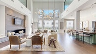 Located at 777 Dunlavy St in Houston's vibrant Montrose neighborhood, this single-story leasing office and amenity space offers a polished, contemporary environment designed to impress. The centerpiece of the space is a grand, double-height lounge area bathed in natural light from floor-to-ceiling windows that frame views of the surrounding pool and courtyard. Soaring white walls are anchored by a striking tile-clad fireplace wall with built-in display shelving and a mounted flat-screen TV. An elaborate branch-inspired chandelier crowns the seating area, where curated furnishings—including curved sofas, woven accent chairs, and layered area rugs over rich hardwood flooring—create a warm, refined atmosphere. Adjacent to the main lounge, a well-appointed refreshment bar features sage-green cabinetry, a sleek stone countertop with bar seating, and professional-grade beverage equipment. Private offices enclosed by floor-to-ceiling glass partitions and black-framed doors provide functional workspaces filled with natural light and outfitted with contemporary furnishings and botanical artwork. A connecting corridor leads to additional workstations with built-in cabinetry and dual monitors. Throughout, the consistent use of hardwood flooring, neutral tones, and carefully selected décor establishes a cohesive, sophisticated aesthetic that is both welcoming and highly functional.