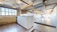 Located at 2400 S Ervay St in Dallas, TX, this industrial-style loft delivers a striking blend of raw architectural character and modern functionality. The open-plan living and dining area is expansive, defined by exposed concrete ceilings with visible structural beams, copper and galvanized pipe runs, and industrial pendant lighting. A continuous row of large factory-style windows lines the main living space, flooding the interior with natural light and framing panoramic views of the Dallas skyline. Corrugated metal wainscoting and polished wood-look flooring reinforce the building's converted industrial heritage throughout.

The kitchen is anchored by a central island with a stainless steel countertop and integrated sink, complemented by a dishwasher and ample cabinetry. The generously sized bedroom features a built-in clothing rail against a dark corrugated accent wall, with additional factory windows bringing in natural light. The bathroom is clean and functional, finished with wood-look tile flooring, a vanity with mirror, and a gridded window. A dedicated laundry area with utility hookups and a water heater rounds out the layout. Ceiling fans installed throughout provide additional comfort in this distinctly urban, loft-style residence.
