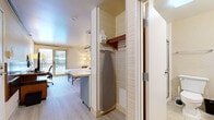 Located at 3200 S Lincoln Ave in Steamboat Springs, Colorado, this well-appointed studio offers a compact yet functional layout designed to maximize every square foot. The main living area features light wood-look flooring, warm neutral tones, and a distinctive accent wall with a botanical print pattern that adds character to the space. Two twin beds are neatly arranged with individual nightstands and lamps, complemented by a wall-mounted split HVAC unit for year-round climate control. The kitchenette is efficiently outfitted with a stainless steel refrigerator, microwave, oven, cooktop, sink with modern fixtures, and light wood countertops — providing all the essentials for self-sufficient living. A stainless steel utility shelf offers additional storage and workspace. A closet with a built-in shelf, clothing rod, and ironing board adds practical convenience. The bathroom features tile flooring, a granite-topped vanity with an undermount sink, a large framed mirror, and a shower/tub combination. A private balcony extends the living space outdoors, offering sweeping views of snow-capped mountains and evergreen-lined surroundings — a true highlight of this Steamboat Springs retreat.