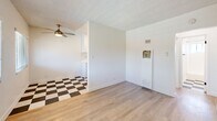 Located at 11635 Downey Avenue in Downey, CA, this single-story, one-bedroom, one-bathroom unit offers a thoughtfully organized layout across a cozy footprint. The interior is finished with light-toned wood laminate flooring throughout the main living areas, creating a warm and cohesive aesthetic that complements the bright white walls.

The living room is an open, airy space featuring a textured ceiling and a ceiling fan with integrated lighting, providing both comfort and airflow. Natural light filters in through a window fitted with horizontal blinds, illuminating the room's clean, minimalist character. A distinctive black-and-white checkered tile floor transitions into the kitchen area, offering a charming visual contrast and clearly delineating the two spaces.

The bedroom is a well-proportioned private retreat, also featuring light wood flooring, white walls, and a ceiling fan. It connects seamlessly to the hallway, maintaining the unit's efficient flow.

The bathroom is neatly appointed with a white tub-shower combination, a rain-style showerhead with chrome fixtures, and a white vanity with an integrated sink. A small window above the tub brings in natural light, keeping the space bright and fresh.

A connecting hallway ties all rooms together, contributing to the unit's practical and streamlined layout. Overall, the space presents a clean, move-in-ready environment with a simple, functional design.