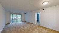 Located at 4002 Sharon Park Lane in Sharonville, Ohio, this 2-bedroom, 1-bathroom residence presents a functional single-floor layout designed for comfortable everyday living. The living room is a welcoming, open space featuring wall-to-wall carpeting and a large sliding glass door fitted with vertical blinds, allowing natural light to flow in while providing a view of the surrounding greenery outside. The layout connects seamlessly to a hallway that leads to the private quarters of the home. Both bedrooms are carpeted and feature clean white walls, creating a bright and neutral atmosphere. The primary bedroom is a well-proportioned room equipped with two sliding closet doors, offering generous storage. The second bedroom also includes a closet and a window that brings in natural daylight. The full bathroom is finished with wood-look vinyl flooring and includes a tiled shower-tub combination with a chrome fixture, a toilet, and a towel bar, maintaining a clean and functional aesthetic. Throughout the home, the consistent use of neutral tones and carpet provides a cohesive, understated look. The unit's compact yet efficient footprint makes it a practical choice for those seeking straightforward, low-maintenance living in Sharonville.