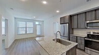 This thoughtfully designed single-floor residence showcases a contemporary open-concept layout that seamlessly connects the kitchen, dining, and living areas. The kitchen serves as the centerpiece, equipped with a large granite-topped island featuring an undermount sink, dark wood-tone cabinetry, a full suite of stainless steel appliances including a refrigerator, range, and microwave, and a classic subway tile backsplash. Recessed lighting and wood-look plank flooring extend throughout the main living area, which is bathed in natural light from oversized windows with blinds. Built-in shelving near the entryway adds practical storage and display options. The bedrooms are well-proportioned, featuring the same wood-look flooring, neutral white walls, and windows that invite natural light. One bedroom includes a ceiling fan for added comfort. The bathrooms are finished with granite vanity countertops, dark cabinetry, and marble-style tile surrounds in the soaking tub and shower areas. Consistent use of quality finishes — including brushed nickel fixtures and clean, crisp millwork — creates a cohesive and polished aesthetic throughout the entire space.