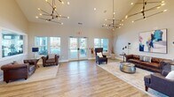 Located at 2101 Country Squire Ct in West Lafayette, Indiana, this single-floor community amenity facility offers a well-appointed and thoughtfully designed space for residents. The welcoming lounge area immediately impresses with soaring vaulted ceilings, light hardwood flooring, and a pair of striking sculptural chandeliers that cast a warm, ambient glow. Comfortable leather and upholstered seating arrangements are complemented by large windows and glass double doors that flood the space with natural light and provide views of the outdoor surroundings.

A hallway connects the lounge to the remaining areas of the facility, passing a convenient kitchenette station outfitted with dark wood cabinetry, a countertop sink, and a smart package or beverage kiosk — all accented by an industrial pendant light. Restrooms are accessible directly off this corridor.

The expansive exercise room is the centerpiece of the fitness offerings, divided into two well-equipped zones. The cardio area features multiple treadmills, ellipticals, stationary bikes, and strength machines, all oriented toward large windows and wall-mounted TVs, with ceiling fans maintaining air circulation. The functional training zone includes cable machines, medicine balls, resistance equipment, a wall-mounted boxing pad, and a bench, providing a comprehensive workout environment. Neutral carpet flooring and recessed lighting complete the clean, professional aesthetic throughout.