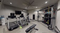 This two-floor fitness space is thoughtfully designed to accommodate a comprehensive range of workout disciplines. The lower level serves as the primary strength and cardio zone, featuring durable rubber flooring, recessed lighting, and a large ceiling fan paired with a wall-mounted mini-split system for climate control. Equipment includes multiple treadmills, an elliptical, a flat weight bench, a full dumbbell rack, and a wall-mounted flat-screen TV. An Octagon functional training rig anchors one wall, complete with a heavy punching bag, resistance attachments, and organized storage for medicine balls, battle ropes, and accessories. A dramatic spiral staircase with sleek black metal railings connects the two levels, serving as both a functional and architectural centerpiece.

The upper level transitions to lighter wood-look flooring and an airier atmosphere, also equipped with a ceiling fan and mini-split unit. This floor is dedicated to cycling and functional training, housing several Spinning bikes and balance and stability equipment. A large, vibrant wall mural featuring an abstract peacock design adds an energetic focal point, complemented by a wall-mounted TV and mirrored doors. Together, both floors create a cohesive, well-equipped private fitness environment.