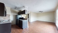 This single-floor, 2-bedroom, 2-bathroom unit offers a practical and comfortable layout designed for everyday living. The open-concept living area is highlighted by warm hardwood-style flooring that extends throughout the unit, creating a cohesive and inviting atmosphere. A ceiling fan with a light fixture anchors the living room, which receives natural light through a large window fitted with blinds. The front entry door opens directly into this spacious common area, which flows seamlessly toward the kitchen.

The kitchen features dark cabinetry, a stone-tile backsplash, granite-style countertops, and black appliances, including a range and refrigerator. A peninsula counter separates the kitchen from the living space, providing a convenient breakfast bar area. An overhead range hood adds a functional focal point to the kitchen.

Both bedrooms carry the same hardwood-style flooring and are equipped with ceiling fans. Each room includes a window with blinds that allows natural light while maintaining privacy. The bedrooms offer closet storage, with at least one featuring a reach-in closet with a built-in rod. Neutral wall tones throughout the unit contribute to a clean, versatile aesthetic that accommodates a variety of furnishing styles. Textured ceilings are present in the common areas of the unit.