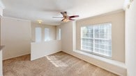 This single-floor residence offers a thoughtfully designed layout that balances comfort and functionality. The living area is a welcoming, carpeted space bathed in natural light from large windows fitted with blinds. A ceiling fan with integrated lighting keeps the room comfortable year-round, while crown molding adds a refined touch. A pass-through opening connects the living area directly to the kitchen, enhancing the open feel of the space.

The galley-style kitchen is efficiently arranged with warm wood-toned cabinetry lining both sides, offering generous storage. It is equipped with a full suite of white appliances, including a coil-top range, built-in microwave, refrigerator, and dishwasher. Light hardwood-style flooring runs throughout, and a door leads to additional utility space.

The bedroom continues the warm, carpeted aesthetic and features its own ceiling fan, a large window that invites natural light, and access to a spacious walk-in closet outfitted with multi-tiered wire shelving and hanging rods for ample organization.

The bathroom is clean and classic in design, featuring a full-size soaking tub with a tiled surround, a shower rod, and a wood-cabinet overhead storage unit. The overall ambiance of the space is bright, neutral, and move-in ready.