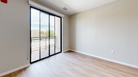This thoughtfully designed single-floor unit offers a clean, contemporary aesthetic throughout its efficiently arranged layout. The open-concept living and kitchen area serves as the heart of the space, anchored by a sleek white island with a built-in sink, integrated microwave, and a linear pendant light overhead. The kitchen is outfitted with stainless steel appliances — including a French door refrigerator and gas range — complemented by white flat-panel cabinetry and a subway tile backsplash. Light hardwood flooring runs throughout the main living area, enhancing the bright, airy atmosphere. A large sliding glass door leads directly to a private balcony, offering open outdoor views and flooding the living space with natural light. The two bedrooms feature plush carpeting and large windows that frame outdoor scenery, providing comfortable, well-lit retreats. The bathroom is finished in a modern style, featuring a white vanity with ample drawer storage, a large mirror with overhead lighting, and matte black accent hardware. Clean neutral wall tones and consistent finishes throughout give the unit a cohesive, move-in-ready feel.
