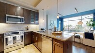 Located in the heart of downtown Austin at 101 Colorado St, this well-appointed one-bedroom, one-bathroom residence offers a thoughtfully designed single-floor layout. A light-filled hallway with travertine tile flooring welcomes you and leads into an expansive open-concept living, dining, and kitchen area. The living room features warm hardwood flooring, bold blue accent walls, track lighting, and floor-to-ceiling sliding glass doors that bathe the space in natural light and open to a private patio with metal railing, lush landscaping, and urban skyline views. The gourmet kitchen is outfitted with rich dark-wood cabinetry, granite countertops, a large center island with pendant lighting, stainless steel appliances, a tile backsplash, and under-cabinet lighting. The serene bedroom continues the bold blue color palette with wood flooring and a window offering natural light. The spa-inspired bathroom features travertine stone tile, a deep soaking tub, a glass-enclosed walk-in shower, and dark-wood vanity cabinetry. Additional highlights include a spacious walk-in closet with built-in shelving, a dedicated utility and laundry room, and a generous outdoor patio perfect for enjoying Austin's vibrant surroundings.