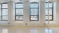 Located at 120 Valley St in Providence's West End, this single-floor loft unit reflects the building's industrial heritage through a thoughtfully converted interior. The main living area is an expansive, open space defined by tall ceilings and a row of large arched windows framed by painted white brick columns. These generational factory windows allow abundant natural light to pour in from multiple directions, offering views of surrounding greenery. Exposed metal ductwork runs overhead alongside track lighting, reinforcing the loft's industrial character.

The kitchen is efficiently laid out in an L-shape and features light maple cabinetry, granite countertops, a stainless sink, and a full suite of white appliances including a gas range, dishwasher, and refrigerator. The bathroom is clean and functional, finished with tile flooring, a full tub/shower combination, and a vanity with granite countertop detailing consistent with the kitchen. A utility area near the entry houses a water heater and additional storage behind louvered doors. Sliding doors within the main space provide flexible room division, enhancing the unit's adaptability for both living and working purposes.