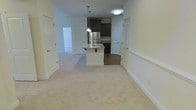 This two-floor residence showcases an open-concept layout that seamlessly connects the living area to the kitchen. The main living space is finished with plush, neutral-toned carpeting that extends throughout, creating a warm and comfortable atmosphere. A transition to hardwood-style flooring marks the kitchen zone, providing a clean visual distinction between the two areas.

The kitchen serves as a functional centerpiece, highlighted by a white kitchen island with a built-in sink, granite-style countertops, and dual pendant lights hanging overhead. Dark espresso cabinetry lines the kitchen walls, offering rich contrast against the light-toned walls and ceiling. A stainless steel refrigerator anchors the space, contributing to the kitchen's modern aesthetic.

The open layout allows for generous sightlines across both the kitchen and living areas, enhancing the overall sense of space. Multiple white panel doors are visible throughout, leading to additional rooms and suggesting a well-distributed floor plan. Recessed and flush-mount ceiling lighting provides consistent illumination throughout. With two floors, this residence offers a functional separation of living and private spaces.