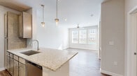 This thoughtfully designed one-bedroom, one-bathroom unit in Shreveport, Louisiana offers an efficient and functional layout with contemporary finishes throughout. The open kitchen and living area serves as the heart of the unit, where a galley-style kitchen impresses with stainless steel appliances, taupe cabinetry extending to the ceiling, granite countertops, a subway tile backsplash, and a pendant-lit island. Wood-look vinyl plank flooring runs throughout the main living areas, adding warmth and durability. A distinctive built-in nook with open shelving, a granite desktop surface, and a subway tile accent provides a versatile workspace or display area. The bedroom is carpeted for comfort, bathed in natural light from multiple windows with slatted blinds, and features a ceiling fan. The bathroom is finished with a full tub and shower combination surrounded by classic white subway tile, wood-look flooring, and overhead cabinetry for storage. Neutral gray walls throughout create a clean, cohesive aesthetic, while the dedicated closet offers practical storage solutions. The unit's overall ambiance is bright, modern, and move-in ready.