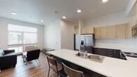 Located at 3230 Kinsrow Ave in Eugene, Oregon, this single-floor unit offers a thoughtfully designed layout with a modern aesthetic throughout. The open-concept kitchen serves as the heart of the space, showcasing a striking two-tone cabinet design with light wood upper cabinets and dark charcoal lower cabinets, complemented by a white subway tile backsplash. Stainless steel appliances — including a French door refrigerator with ice maker, an electric range, and an over-the-range microwave — provide a sleek, functional cooking environment. A generously sized kitchen island with a white countertop and integrated sink doubles as a casual dining area, with bar seating on one side. Wood-look flooring runs throughout the unit, adding warmth and continuity to the space. The living area accommodates comfortable seating and receives natural light through a large window fitted with blinds. Each bedroom is well-proportioned, featuring wood-look flooring, a dedicated closet with sliding doors, a window for natural light, and space for a desk and bed. The bathroom is clean and bright, with a full tub-shower combination featuring white surround panels, chrome fixtures, and a dark-toned vanity. The overall design is clean, contemporary, and functional.