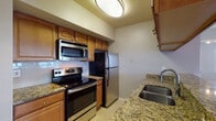 This thoughtfully designed single-floor residence offers a comfortable and functional layout with a range of attractive interior finishes throughout. The open living area is a standout, featuring vaulted ceilings with a ceiling fan, rich hardwood-style flooring, and a striking stone-surround fireplace that serves as the focal point of the room. Multiple windows allow natural light to fill the space, creating a bright and welcoming ambiance.

The kitchen is well-equipped with warm-toned wood cabinetry, granite countertops, a tile backsplash, and a full suite of stainless steel appliances including a range with over-the-range microwave and a refrigerator. A double stainless steel sink adds to the kitchen's practicality.

A sunlit hallway with large windows connects the main living areas to the private quarters. The bedrooms are carpeted for comfort, each featuring ceiling fans and ample natural light. At least one bedroom includes access to a spacious walk-in closet with shelving. The bathroom is outfitted with wood cabinetry, a large vanity mirror with overhead lighting, and a tub-shower combination. Throughout the residence, neutral tones and clean finishes contribute to a cohesive, move-in-ready aesthetic.