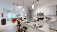 Located at 503 E Stone Ave in Greenville, SC, this 2-bedroom, 3-bathroom residence offers a thoughtfully designed open-concept floor plan with modern finishes throughout. The kitchen serves as a centerpiece, showcasing granite countertops, a spacious peninsula with bar seating, gray shaker-style cabinetry, subway tile backsplash, and stainless steel appliances including a range, microwave, and refrigerator. Pendant lights and track lighting illuminate the space, which flows seamlessly into the living area. The living room features plush carpeting, large windows with sheer draping that invite natural light, and views of the surrounding neighborhood. Both bedrooms are carpeted and well-sized, each benefiting from generous natural light through large windows with blinds and curtains. The primary bedroom includes a walk-in closet with built-in wire shelving for ample storage. The bathrooms are clean and contemporary, featuring white subway tile surrounds and soaking tub-shower combinations with light tile flooring. Wood-look plank flooring runs through the kitchen and entry areas, providing a warm, cohesive aesthetic. The overall ambiance is modern and comfortable, reflecting a neutral palette that offers a versatile and inviting living environment.