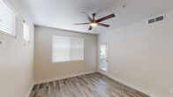 This single-floor residence offers a well-designed layout that balances comfort and functionality throughout its living spaces. The main living areas are finished with durable wood-look plank flooring in a warm gray tone, complemented by crisp white walls and neutral baseboards that create a bright, cohesive aesthetic. Ceiling fans with integrated lighting are installed in the living spaces, providing both air circulation and ambient illumination, while multiple windows dressed with white horizontal blinds invite natural light throughout.

The kitchen is a standout feature, outfitted with white shaker-style cabinetry extending to the upper walls for ample storage, light gray countertops, and a stainless steel sink positioned beneath a window. A full suite of stainless steel appliances — including a refrigerator, electric range, and over-the-range microwave — adds a modern, cohesive finish. The layout allows for efficient movement and workflow within the space.

A hallway connects the living areas to additional rooms, with an arched doorway leading to a bathroom featuring white cabinetry and a vanity. The overall floor plan, visible in the aerial model view, reveals a thoughtfully arranged single-level layout with clear separation between the kitchen, living, and private areas. The space presents a clean, move-in-ready environment with consistent modern finishes throughout.