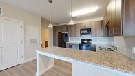 Located at 1140 Bridgefield Pl in Charlotte, NC, this 2-bedroom, 1-bathroom residence offers a well-designed single-floor layout. The open-concept kitchen and living area forms the heart of the home, where a granite-topped peninsula island serves as the central gathering point. The kitchen is outfitted with rich dark wood cabinetry, a white subway tile backsplash, black appliances including a refrigerator, electric range, built-in microwave, and dishwasher, all set atop light hardwood-style flooring. Pendant lighting above the island adds a polished finishing touch. The living room features a ceiling fan, light-toned flooring, and a glass door that opens to a balcony, allowing natural light to flow freely into the space. Both bedrooms are carpeted and neutral in tone, each offering a closet with built-in shelving for organized storage. The primary bedroom is a comfortable, well-proportioned space with a large window offering exterior views. The bathroom echoes the home's consistent design language, with matching dark wood cabinetry, a granite vanity top, light wood-look tile flooring, and a wall-mounted mirror. Clean lines and a neutral color palette create a cohesive, modern ambiance throughout.