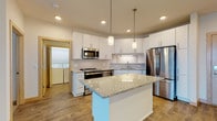 Located at 3601 Cross Hill Dr in Madison, Wisconsin, this single-floor residence offers a clean, modern design with an open-concept living and kitchen area. The kitchen is a standout feature, showcasing crisp white shaker cabinetry, granite countertops, a subway tile backsplash, and a full suite of stainless steel appliances including a French door refrigerator, range, microwave, and dishwasher. A central island with pendant lighting above provides additional prep space and serves as a natural gathering point. Wood-look flooring runs throughout the main living areas, lending warmth and cohesion to the space. The living area is bright and open, with a sliding glass door that allows natural light to fill the room. Bedrooms are carpeted for comfort, with one featuring a walk-in closet and ceiling fan, and another offering a dedicated closet with built-in shelving. The bathroom is well-appointed with granite vanity countertops, a soaking tub with shower, and wood-look tile flooring. A dedicated laundry area with side-by-side washer and dryer hookups adds everyday convenience to this thoughtfully designed home.