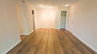 This single-floor space is designed with a clean, open layout that maximizes functionality and ease of movement. The main living area is finished with warm-toned hardwood flooring that runs throughout, lending the space a classic yet modern character. A track lighting fixture mounted on the ceiling provides adjustable, focused illumination, complementing the neutral cream-toned walls that create a bright and airy atmosphere.

A doorway on one side leads into what appears to be a kitchen area, where a refrigerator is visible, indicating a well-positioned food preparation space conveniently accessible from the main living area. On the opposite side of the room, a walk-in closet offers notable storage capacity, with a visible shelving and rod system ideal for organized storage. An additional door, likely leading to an entryway or secondary room, is positioned nearby.

The textured ceiling adds subtle visual depth, while the wide-plank hardwood floors serve as a standout architectural feature that ties the space together cohesively. The overall ambiance is clean, neutral, and move-in ready, offering a versatile canvas suited to a variety of interior styles.