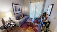 This single-story residence offers a thoughtfully designed layout that balances functionality with contemporary style. The living area serves as the heart of the unit, featuring crown molding, a ceiling fan, and a sliding glass door framed by vertical blinds that allows natural light to fill the space and provides access to the outdoors. Warm hardwood-style flooring anchors the room, complemented by neutral wall tones.

The kitchen is well-equipped with dark cabinetry, granite countertops, stainless steel appliances including a refrigerator, microwave, and range, and a peninsula with an integrated sink that doubles as a breakfast bar with pendant lighting overhead. A set of double doors provides additional storage or pantry space nearby.

The bedroom is carpeted and comfortably sized, featuring a ceiling fan, natural light from a window with blinds and curtain panels, and ample room for furnishings. The bathroom is finished with dark wood cabinetry, granite countertops, a single vanity sink, tile flooring, and a tub-shower combination with a tiled surround, offering a clean and functional design throughout.