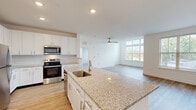 Located at 34 Silverado Circle in Hoschton, GA, this well-appointed single-floor residence offers a thoughtfully designed open-concept layout that maximizes both functionality and comfort. The combined kitchen and living area serves as the heart of the home, anchored by a substantial granite-topped island with an undermount sink, crisp white shaker cabinetry, a classic subway tile backsplash, and a full suite of stainless steel appliances including a refrigerator, electric range, and microwave. Light wood-style flooring runs throughout the main living areas, complementing the bright, neutral color palette. Large multi-pane windows flood the living room with natural light and provide views of the surrounding landscape, while a ceiling fan adds to the room's comfort. The spacious bedroom features plush carpeting and a dedicated window that brings in additional natural light. A generously sized walk-in closet with dual wire shelving systems and hanging rods provides ample storage. The bathroom is finished with a white vanity, granite countertop, a framed mirror, and light wood-style flooring, maintaining the cohesive aesthetic found throughout the home. Clean lines, consistent finishes, and an abundance of natural light give this residence a bright, modern ambiance.