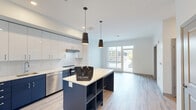 Located at 2695 S Water St in Pittsburgh's South Side neighborhood, this contemporary 2-bedroom, 2-bathroom residence at The Park offers a thoughtfully designed single-floor layout with modern finishes throughout. The open-concept kitchen and living area serves as the heart of the home, anchored by a striking navy blue kitchen island with built-in shelving beneath a white quartz countertop and pendant lighting. The kitchen features two-tone cabinetry — crisp white uppers paired with navy lowers — along with stainless steel appliances including a dishwasher, range, refrigerator, and microwave. Light wood-look flooring runs throughout, complementing the clean, neutral color palette. Large sliding glass doors in the living area flood the space with natural light and open directly onto an outdoor patio, seamlessly blending indoor and outdoor living. The spacious primary bedroom offers a comfortable retreat, while the second bedroom features a natural light-filled window and ample closet space with sliding doors. The two bathrooms are well-appointed: one features a glass-enclosed walk-in shower with built-in shelving, while the other includes a soaking tub with shower and open shelving for added storage. A dedicated closet rounds out this efficient and stylish residence.