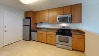 Located at 158 Concord Rd in Billerica, Massachusetts, this single-floor unit offers a practical and comfortable layout designed for everyday living. The open living area is finished with plush carpeting and features a sliding glass door that fills the space with natural light while providing direct access to an outdoor green area with neighborhood views. A large multi-pane window in the bedroom continues the theme of natural light, complemented by baseboard heating throughout. The bedroom is generously sized and includes a walk-in closet with built-in shelving, offering ample storage. The kitchen is well-appointed with warm honey-toned wood cabinetry extending to the ceiling, dark granite-style countertops, a stainless steel sink, and a full suite of stainless steel appliances including a gas range, over-the-range microwave, dishwasher, and refrigerator. Light tile flooring grounds the kitchen space. The bathroom features clean white cabinetry, a single vanity with a large mirror, tile flooring, and a full bathtub with beige tile surround. The overall interior presents a neutral, move-in-ready palette with a straightforward, functional design throughout.