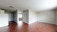 This single-floor unit presents a practical and cohesive layout unified by rich, dark hardwood-style flooring and neutral gray walls throughout. The open living area is generously proportioned, receiving natural light through windows fitted with blinds, and is equipped with a wall-mounted HVAC unit for climate control. A front entry door with a paneled design provides direct access to the main living space.

The kitchen features white cabinetry, granite-style countertops, and a white electric range, maintaining a clean, functional aesthetic. A secondary door in the kitchen offers additional entry or exit access.

The bedrooms are well-sized, each equipped with ceiling fans and windows that bring in natural light and outdoor views. Ample storage is provided through a combination of standard closets and louvered bi-fold closet doors. One bedroom features two separate closets, enhancing storage capacity.

The bathroom is finished with white subway tile surrounding a full soaking tub and shower combination, complemented by chrome fixtures, creating a clean and timeless look. Throughout the unit, bright white trim and baseboards provide a crisp contrast to the warm flooring, contributing to an overall tidy and move-in-ready atmosphere.