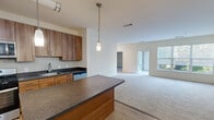 Located at 8 Norden Place in Norwalk, Connecticut, this well-appointed single-floor residence offers a thoughtfully designed layout encompassing one bedroom and one bathroom. The entry opens into a generous kitchen and living area, where light hardwood flooring anchors the kitchen space before transitioning to plush carpet in the living room. The kitchen is a standout feature, showcasing warm wood cabinetry, dark granite-style countertops, a subway tile backsplash, and a central island with pendant lighting overhead. Stainless steel appliances — including a gas range, microwave, refrigerator, and dishwasher — complete the functional and stylish cooking space. The open-concept living area is bright and spacious, benefiting from natural light through large windows and access to a private patio that overlooks a landscaped courtyard with mature trees and a community seating area. The bedroom is generously proportioned, featuring wide windows with garden views and soft carpeting, complemented by a dedicated walk-in closet outfitted with wire shelving for ample storage. The bathroom offers a full tub-shower combination with tile surround, a single vanity with wood cabinetry, and a well-lit mirror. The overall ambiance is clean, modern, and move-in ready.