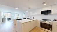 Located at 95 Anderson Street in Hackensack, NJ, this modern 2-bedroom residence offers a thoughtfully designed single-floor layout that maximizes both functionality and style. The open-concept kitchen and living area serves as the heart of the home, anchored by a striking marble-finish waterfall island with bar seating — ideal for casual dining or entertaining. The kitchen is outfitted with high-gloss white cabinetry extending to the ceiling, a textured tile backsplash, stainless steel appliances including a French door refrigerator and gas range, and a professional-style pull-down faucet. Light oak hardwood flooring flows throughout, complementing the clean, all-white palette. The living area is bathed in natural light from large windows, creating an open and airy ambiance. A dedicated dining space adjoins the living room seamlessly. The primary bedroom is a serene retreat featuring multiple windows with street views, a large wall-mounted mirror, and warm natural light. The second bedroom mirrors the same bright, minimalist aesthetic. Throughout the residence, the design is characterized by clean lines, neutral tones, and modern finishes that come together to create a cohesive, contemporary living environment.