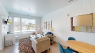 Located in the heart of downtown Columbus, Ohio, this thoughtfully designed single-floor unit offers a bright and contemporary living experience. The open-concept living and dining area is anchored by large windows that frame city skyline views, flooding the space with natural light. Light wood-tone flooring runs throughout, complementing the clean white walls and providing a warm, modern aesthetic. The living area comfortably accommodates a full seating arrangement, with recessed lighting and bold geometric artwork adding visual interest.

The dining area flows seamlessly from the living space, featuring a round wood table with teal accent chairs beneath a pendant light. Adjacent to the dining area, the kitchen is well-appointed with two-tone cabinetry — crisp white uppers and soft gray lowers — paired with white subway tile backsplash, white countertops, a stainless steel sink, and black Whirlpool appliances including an electric range and over-the-range microwave.

The bedroom is a calm, light-filled retreat with a window allowing natural light, ample closet space, and hardwood flooring. The bathroom offers a clean, functional walk-in shower with built-in shelving and a glass panel enclosure. Overall, the space presents a polished, urban-contemporary feel well-suited to downtown Columbus living.
