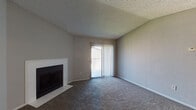 This single-story residence offers a practical and straightforward layout designed for comfortable everyday living. The living room serves as the central gathering space, finished with wall-to-wall carpet in a neutral gray-brown tone and anchored by a white tile-surround fireplace. A sliding glass door fitted with vertical blinds opens to an outdoor patio area, allowing natural light to fill the room. The vaulted ceiling adds a sense of openness, and a textured finish is present throughout the ceiling surfaces.

The galley-style kitchen features dark cabinetry on both sides, white countertops, wood-look flooring, a built-in dishwasher, and a coil electric range. A white subway tile backsplash adds a clean, classic detail to the cooking area.

The bedrooms are carpeted and finished with the same neutral wall tones seen throughout the unit. Each room benefits from natural light provided by windows with horizontal blinds. One bedroom includes a closet with bifold doors, offering practical storage space. The entry area features a ceiling fan and transitions smoothly into the main living space.

The bathroom includes a tiled tub-shower combination, wood-look flooring, and a vanity with a light stone-finish countertop, completing this well-appointed single-level home.