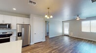 This single-floor home offers a thoughtfully designed open-concept layout that connects the living, dining, and kitchen areas seamlessly. Rich wood-look flooring runs throughout, providing a warm and cohesive aesthetic across every room. The living and dining area is anchored by an elegant brass chandelier and benefits from natural light streaming through multiple windows with blinds.

The kitchen is a functional highlight, featuring crisp white shaker-style cabinetry, light solid-surface countertops, stainless steel appliances including a refrigerator, dishwasher, and range, as well as a central island that adds both prep space and visual appeal. Recessed lighting and a window above the sink keep the space bright and inviting.

The bedrooms are generously proportioned, each equipped with a ceiling fan and natural light from windows overlooking the exterior. Neutral wall tones and consistent flooring create a calm, restful atmosphere throughout.

The bathroom is clean and modern, boasting a wide double-sink vanity with white cabinetry, bright overhead lighting, and direct access to a spacious walk-in closet with built-in shelving. The overall design of this home prioritizes functionality and contemporary style in equal measure.