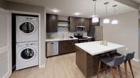 This well-appointed two-bedroom, two-bathroom residence is designed with a modern aesthetic and functional layout across a single floor. The open-concept living area features light wood-style flooring, neutral toned walls, and large windows that invite natural light while offering elevated views of the surrounding urban neighborhood. The contemporary kitchen is equipped with stainless steel appliances, including a refrigerator, electric range, microwave, and dishwasher, all complemented by rich dark cabinetry, light countertops, and a tile backsplash. A kitchen island provides additional prep and dining space. Conveniently located within the kitchen area is a stacked in-unit washer and dryer. Both bedrooms are carpeted and generously sized, each offering access to natural light. The primary bedroom features large corner windows with city views and connects to a walk-in closet and an en-suite bathroom. The second bedroom is a comfortable, well-proportioned room suitable as a guest room or home office. Both bathrooms include a soaking tub and shower combination, vanity with ample storage, and clean tile finishes. Throughout the residence, the design emphasizes a cohesive, contemporary style with neutral tones and practical finishes.