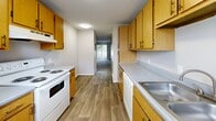 Located at 2726 S Emporia St in Wichita, KS, this two-bedroom unit offers a practical and well-organized single-floor layout. The galley-style kitchen is efficiently designed with warm honey-toned wood cabinetry lining both walls, gray laminate countertops, a double-basin stainless steel sink, and white appliances including a range and refrigerator. Wood-look vinyl flooring runs throughout the kitchen, and a window allows natural light to brighten the space. A textured ceiling adds a classic touch found consistently throughout the unit. The primary bedroom is generously sized, featuring soft carpeting, a ceiling fan with light fixture, a window overlooking the surrounding neighborhood, and direct access to a private bathroom. A closet provides additional in-room storage. The second bedroom is similarly appointed with plush carpet, a window bringing in natural light, and a closet for storage — making it well-suited as a guest room or home office. Both bedrooms are finished in neutral tones, creating a calm and versatile backdrop. The overall layout, as seen in the dollhouse view, is compact yet well-structured, with clearly defined living zones that maximize the use of available space throughout the home.