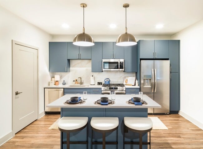 Chef-inspired kitchen with premium finishes, including painted cabinetry, stone-inspired surfaces, stainless steel appliances, and statement pendant lighting. - Modera Westside Trail