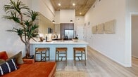 Located at 1050 N Broadway in Denver, CO, this one-bedroom, two-bathroom unit offers a thoughtfully designed layout across a single floor. Dramatic soaring ceilings with an exposed concrete finish define the open living and kitchen area, creating an airy, loft-inspired atmosphere despite the efficient footprint. Large floor-to-ceiling windows flood the living space with natural light and frame views of the surrounding Denver skyline, while a glass-panel door provides access to a private balcony.

The kitchen is outfitted with stainless steel appliances, including a French-door refrigerator, electric range, and built-in microwave. Two-tone cabinetry in light wood and walnut tones pairs with white quartz countertops and a subway tile backsplash. A peninsula with bar seating connects the kitchen to the living area. Light-toned hardwood-style flooring runs throughout the main living spaces.

The bedroom features tall windows with expansive city views and includes an attached walk-in closet. Both bathrooms are finished with white tile, warm wood vanity cabinetry, and white quartz countertops. One bathroom features a soaking tub with vertically stacked white tile surround and chrome fixtures. The overall aesthetic is modern and cohesive throughout.
