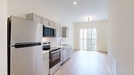Located at 700 E. Long St. in Columbus, Ohio, this one-bedroom, one-bathroom unit offers a well-designed layout that maximizes every square foot of its compact footprint. The open-concept kitchen and living area is anchored by light wood-tone flooring that runs throughout the main space, creating a bright and cohesive atmosphere. The kitchen is equipped with stainless steel appliances — including a refrigerator, electric range, built-in microwave, and dishwasher — complemented by gray shaker-style cabinetry and a classic white subway tile backsplash. A sliding glass door at the end of the living area allows natural light to pour in while providing an outdoor connection. The bedroom is carpeted for comfort and features a generous walk-in closet with dual hanging rods and shelving for ample storage. The bathroom is finished with warm wood-tone flooring, a rich forest green vanity with a white countertop, and a backlit frameless mirror that adds a modern, polished touch. Clean white walls and crisp trim throughout the unit contribute to a fresh, contemporary aesthetic, making this a well-appointed and functional living space in the heart of Columbus.