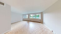 Located at 3450–3460 Rue Drummond in the heart of Montréal, this single-floor unit offers a functional and well-organized layout comprising a living room, kitchen, and bathroom. Throughout the living and bedroom areas, classic parquet flooring laid in a basket-weave pattern adds warmth and character to the space. The living room is a bright, open area lined with a wide bank of windows that frame views of a lush, ivy-covered exterior, allowing generous natural light to fill the room. Baseboard heating runs along the window wall, ensuring comfort throughout the seasons. The kitchen features sleek, flat-front white cabinetry extending to the ceiling for ample storage, paired with dark countertops and light tile flooring. A full-size stainless steel refrigerator anchors the space. The exposed backsplash area adds a raw, textural contrast to the otherwise clean, modern cabinetry. The bathroom is finished with large-format beige wall tiles surrounding a full soaking tub and shower, complemented by light floor tiles, a white vanity with a wood-toned countertop, and recessed lighting, creating a calm and neutral aesthetic throughout.