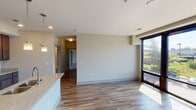 Located at 1011 E Westfield Blvd in Indianapolis, this single-floor unit offers a thoughtfully designed open-concept layout with modern finishes throughout. The kitchen serves as a central focal point, showcasing rich dark-stained cabinetry extending to the ceiling, stainless steel appliances including a refrigerator, electric range, and built-in microwave, and a generous island topped with granite-style countertops and an undermount double sink. Pendant lighting illuminates the island and surrounding space, while recessed ceiling lights provide additional brightness. Wood-look flooring flows through the kitchen and living areas, creating a warm, cohesive aesthetic.

The open living area connects seamlessly to the kitchen and features large windows and a sliding glass door that invite abundant natural light and outdoor views. Bedrooms are finished with plush carpet and windows overlooking the surrounding greenery. The bathrooms are well-appointed with wood-toned vanities, granite-style countertops, framed mirrors, and full tub-shower combinations featuring white subway tile surrounds. An additional half-bath includes a grab bar, indicating accessibility-conscious design. The overall ambiance is clean, contemporary, and move-in ready.