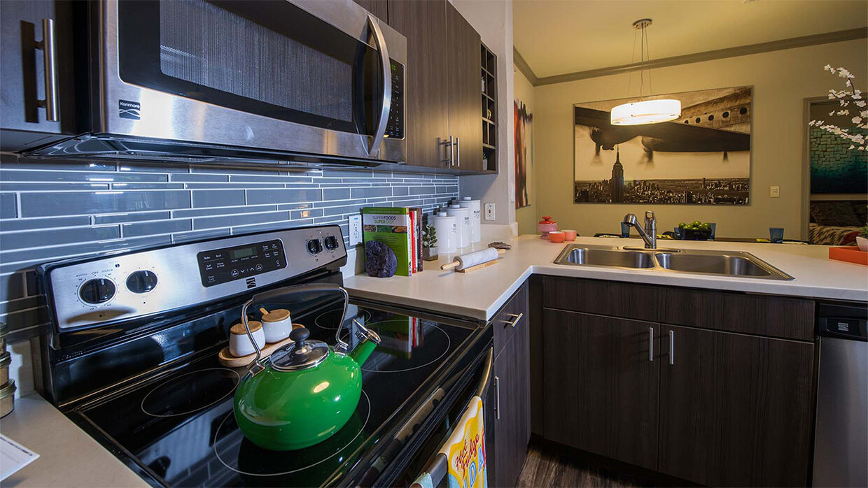 Cocina del apartamento con electrodomésticos de acero inoxidable, encimeras de cuarzo y pisos de madera. - Griffis Lakeline Station