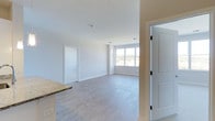 This single-floor, two-bedroom, two-bathroom residence offers a clean and contemporary living environment designed for comfort and functionality. The open-concept living area is immediately welcoming, featuring light hardwood-style flooring that extends throughout the main space, creating a cohesive and airy feel. Crisp white walls and white trim work complement the neutral palette, lending the interior a fresh, move-in-ready aesthetic.

A large window in the living area allows abundant natural light to pour in, offering views of the surrounding greenery and enhancing the sense of openness within the space. Recessed lighting supplements the natural light, ensuring the room remains well-lit at all hours. The living area flows seamlessly from the kitchen, where granite or granite-style countertops are visible, adding a touch of refined detail to the space.

Multiple doorways lead to the two bedrooms and bathrooms, providing a practical layout that promotes privacy and ease of movement. The overall design emphasizes simplicity and brightness, making this residence an inviting and functional home suitable for a variety of lifestyles.