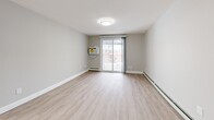 This 2-bedroom, 1-bathroom residence at 144 Dunbarton Rd in Manchester, NH offers a clean, modern layout across a single floor. The combined kitchen and living area serves as the heart of the home, featuring light wood-style flooring, neutral gray walls, and a sliding glass door that opens to a private balcony, filling the space with natural light. The kitchen is well-appointed with crisp white shaker cabinetry, a subway tile backsplash, stainless steel appliances including a refrigerator, dishwasher, and range, and a wall-mounted microwave — all complemented by light wood flooring for a cohesive look. The two bedrooms are carpeted in warm beige tones and painted in soft cream, each equipped with baseboard heating. The spacious primary bedroom benefits from dual windows that invite natural light and outdoor views. The second bedroom features a double-door closet. The full bathroom includes a soaking tub and shower combination with gold-toned fixtures set against clean white surroundings. A hallway connects the rooms efficiently, and the entry area includes an electrical panel. Baseboard heating is present throughout, ensuring comfort year-round.